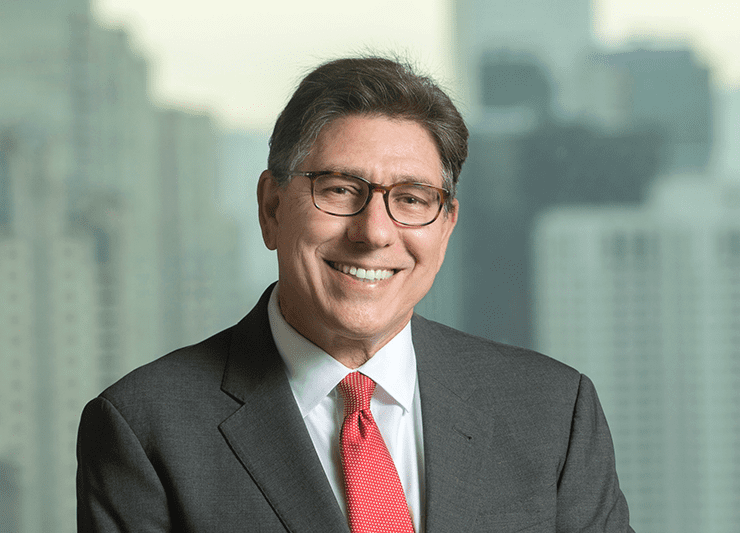 Man wearing glasses and a suit smiling at the camera. Cityscape backdrop